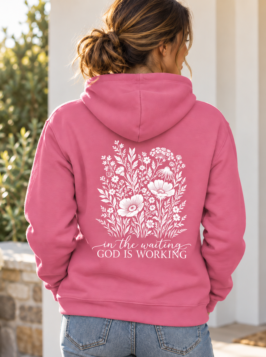 Woman wearing the Pink Lemonade In the Waiting, God Is Working floral hoodie, back view showing the wildflower design