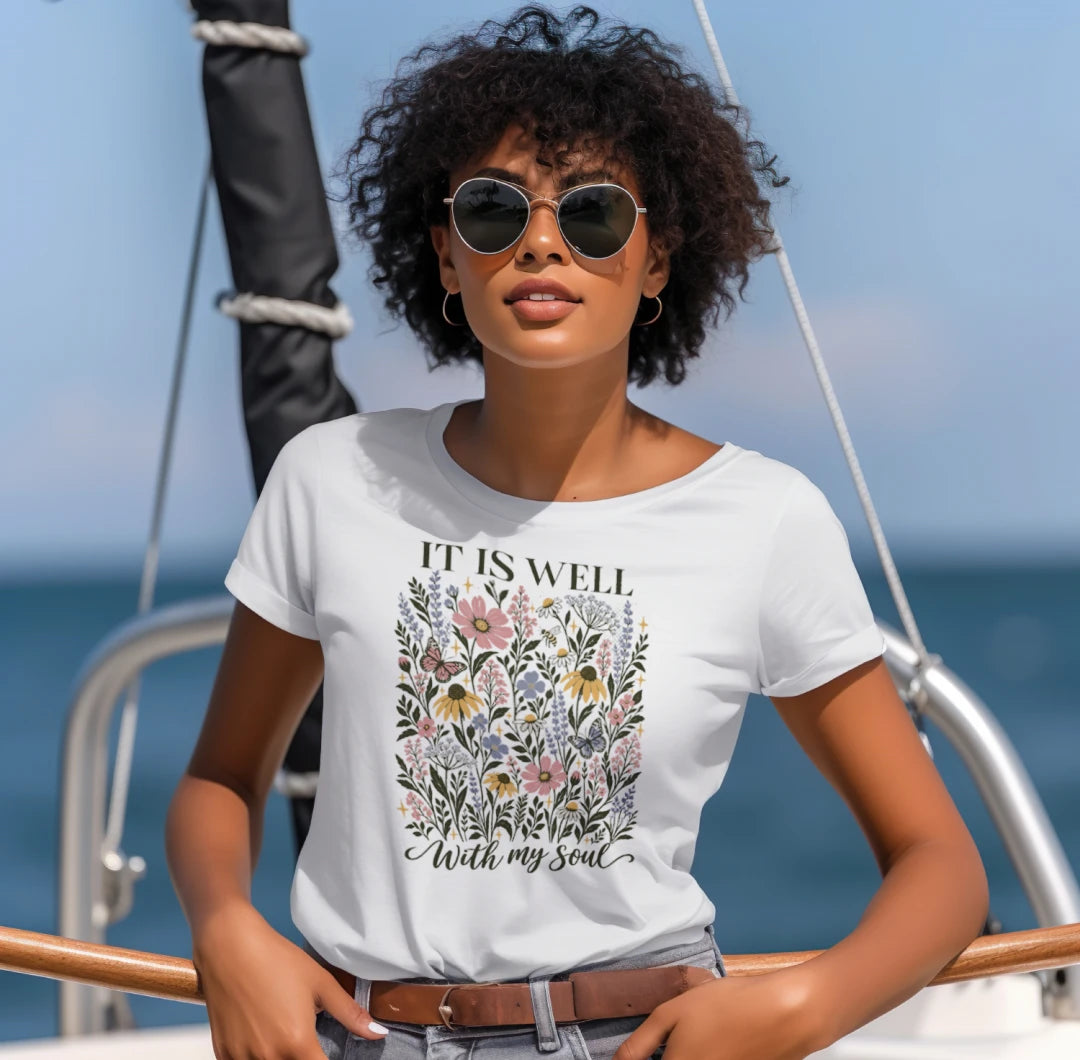 Woman in sunglasses wearing the white It Is Well With My Soul floral tee by the water