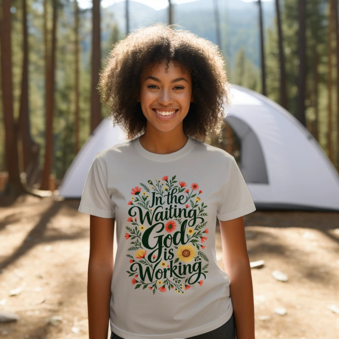 Woman wearing the In the Waiting, God Is Working floral tee outdoors near a tent